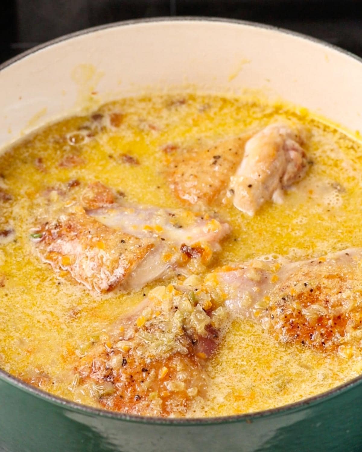 Chicken thighs nestled into the milk and stock braising liquid with fresh herbs.