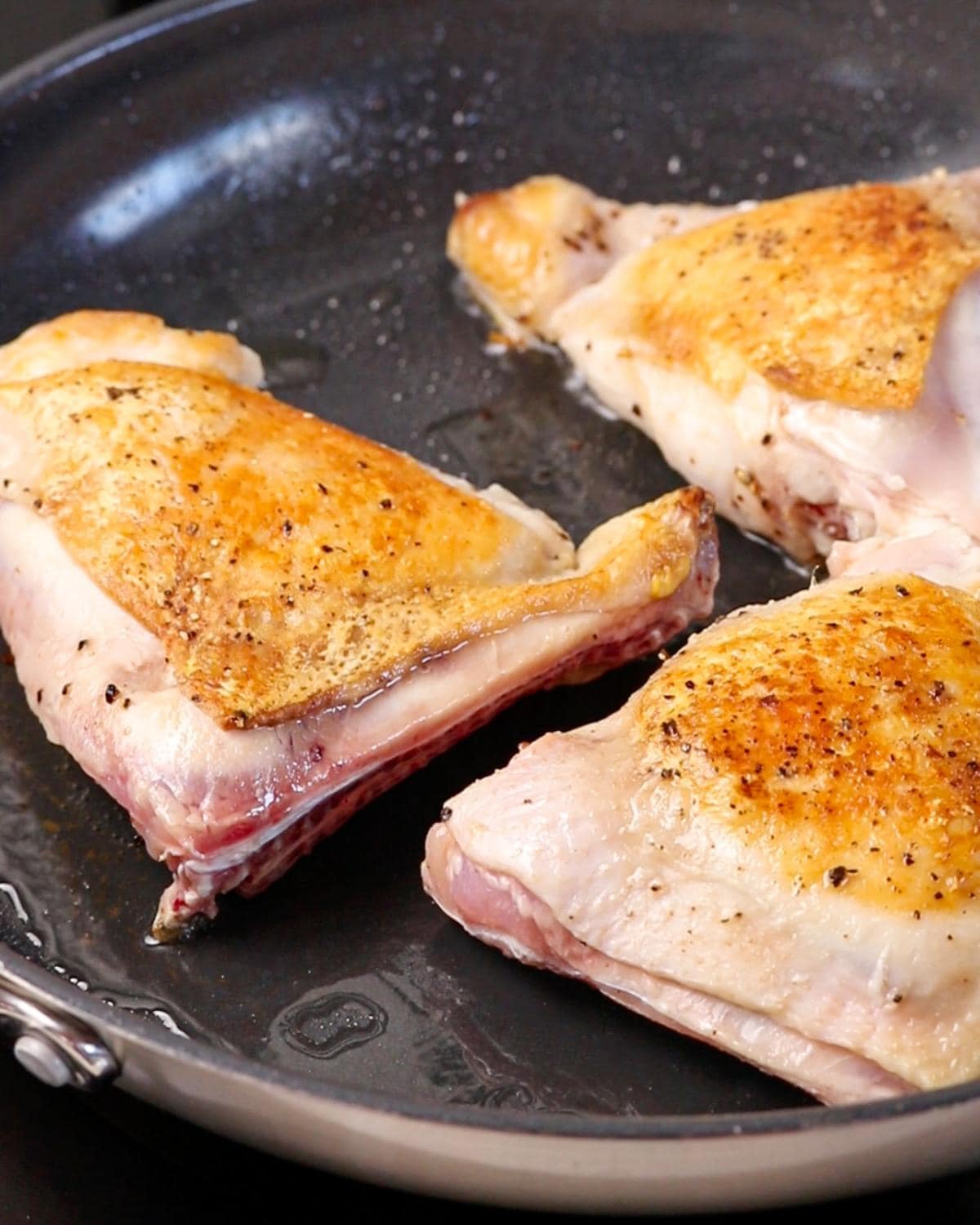 Bone-in chicken thighs browning skin-side down in a frying pan.