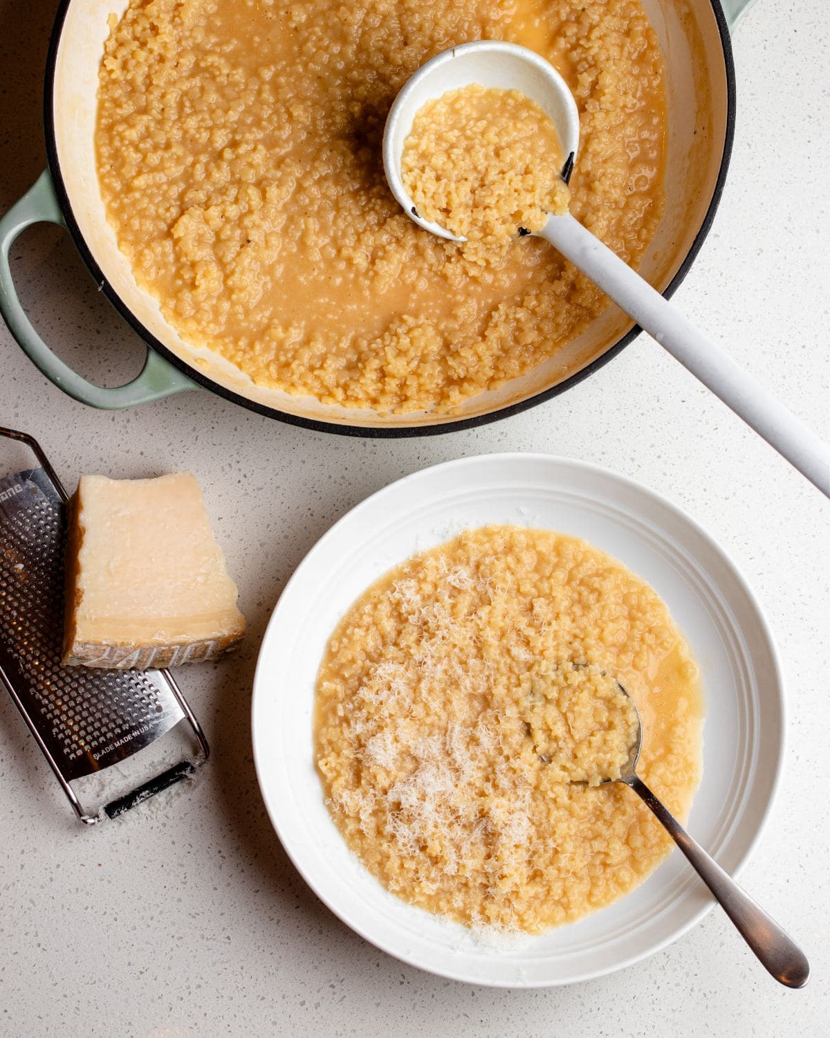 Pastina in a saucepan with ladle and a bowl with pastina served in with a spoon. Parmesan and a grater lying beside.