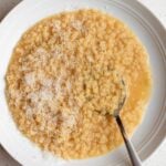 White plate with pastina in stock, grated parmesan cheese on top.