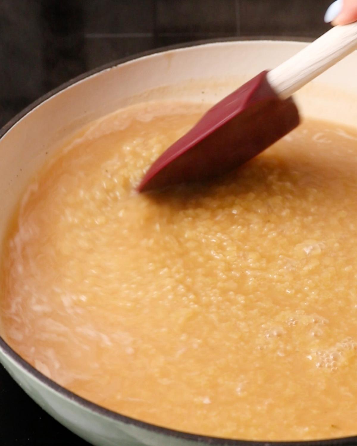 Pastina simmering in chicken stock while being stirred with a spatula.