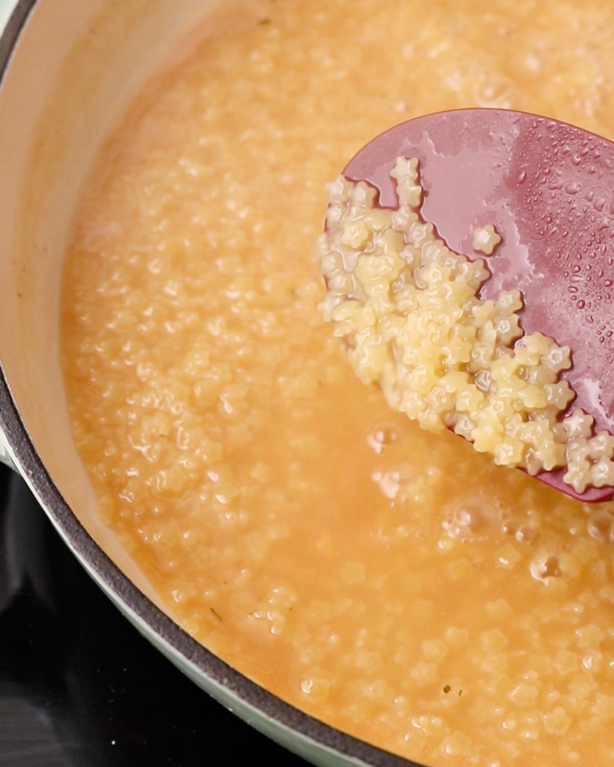 Cooked stelline pastina with a shallow layer of chicken stock remaining in the pan.