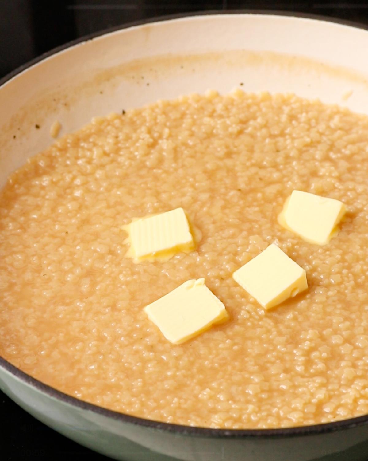 Butter added to cooked pastina in a wide shallow pan.