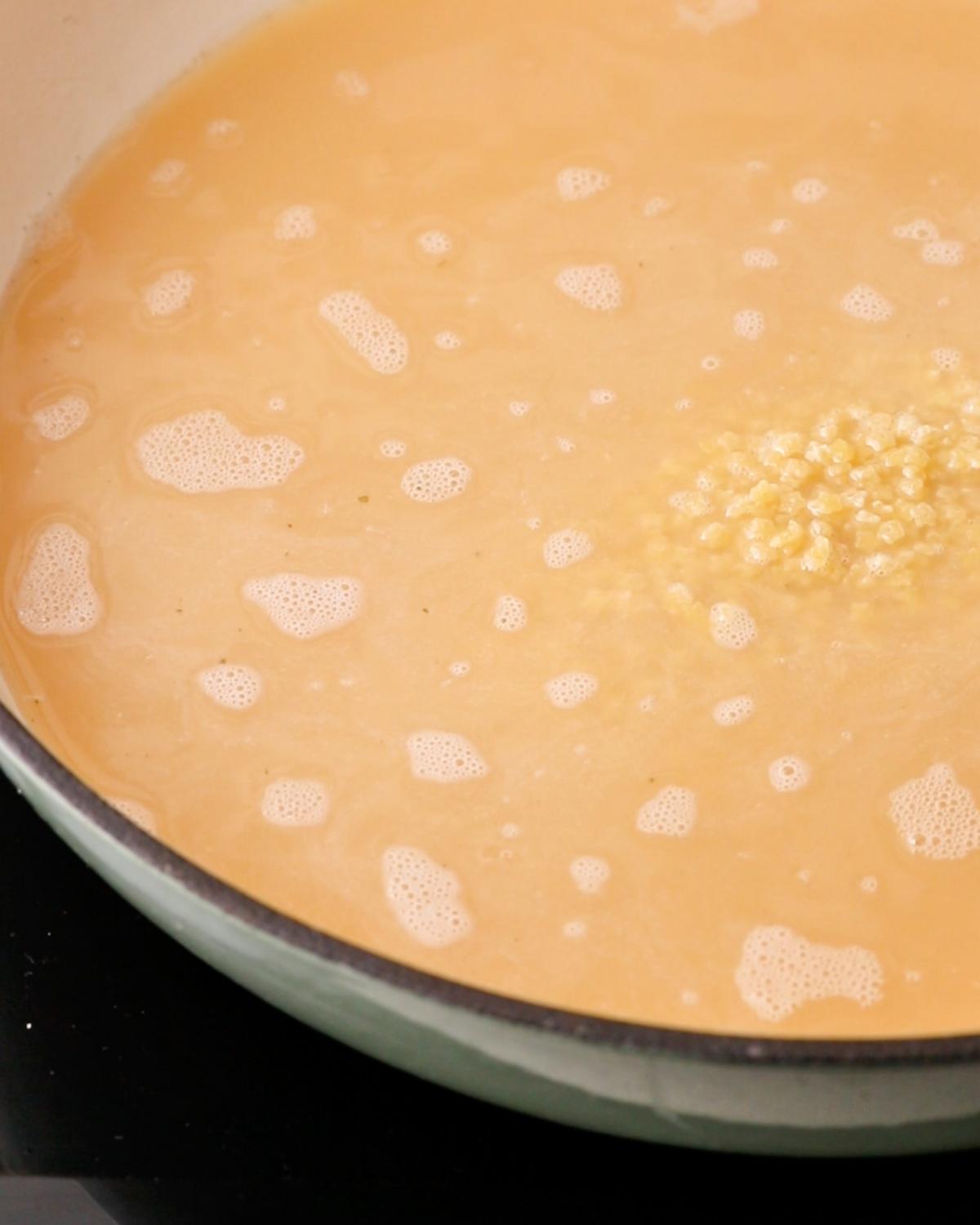 Star-shaped pastina added to chicken stock in a wide shallow pan.